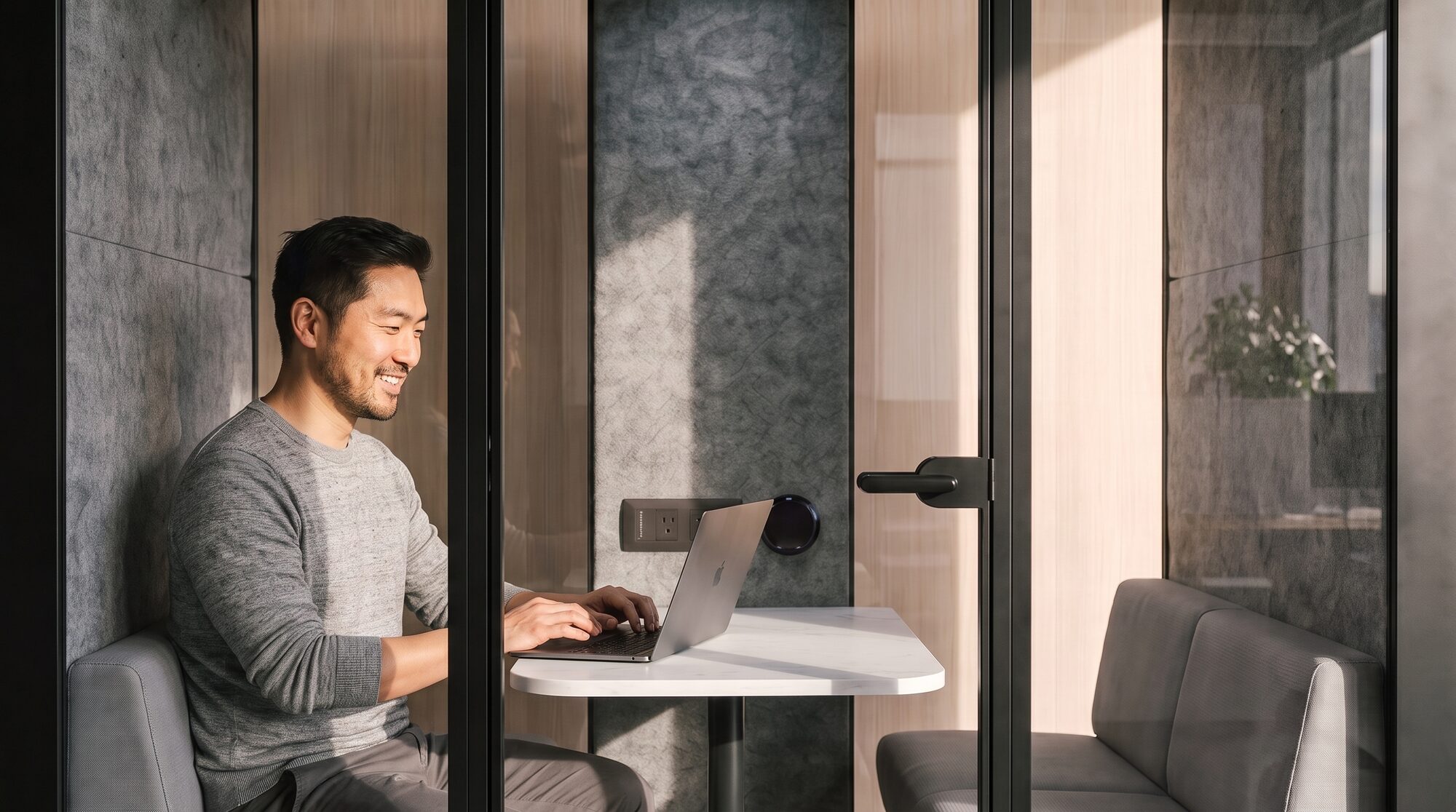 A man working alone inside an enclosed meeting pod, laptop open on a small table.